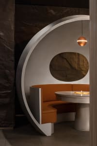 A modern restaurant dining area with a circular wooden table and two chairs, surrounded by clean lines and minimalistic decoration, creating a cozy ambiance