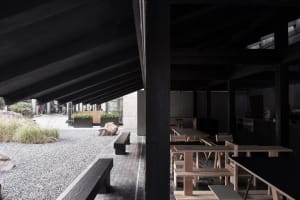 A modern restaurant interior with wooden tables and benches, a black roof, and multiple chairs, creating a warm and inviting atmosphere
