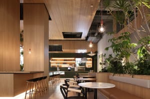 A modern restaurant interior with wooden walls and floors, featuring dining tables, chairs, and potted plants