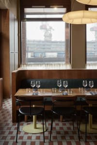 Modern restaurant interior with wooden elements, a brick wall, and wine glasses on tables, creating a warm and inviting atmosphere
