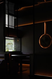 A cozy restaurant dining area with black walls, natural light, and a large table surrounded by chairs