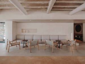 A modern living area with a large couch and chairs arranged around a coffee table, surrounded by concrete walls and a minimalist aesthetic
