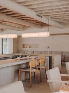 Modern open concept kitchen and dining area with white cabinets, a long dining table, and wine glasses, set against a neutral background
