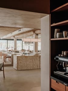 A warm and inviting restaurant dining area with a large wooden table, chairs, and decorative vases, set in a cozy atmosphere with a coffee maker in the background