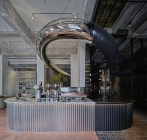 Modern bar area with a counter featuring cups, bottles, and vases, surrounded by potted plants and a stylish atmosphere