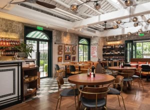 A cozy restaurant interior with multiple tables, chairs, and potted plants, featuring a warm and inviting atmosphere