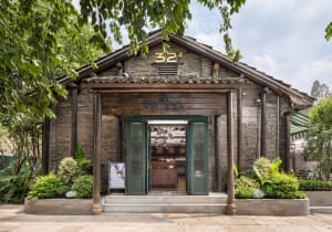 A warm and inviting Asian restaurant with a wooden exterior, green doors, and a spacious dining area with multiple tables and chairs, surrounded by potted plants