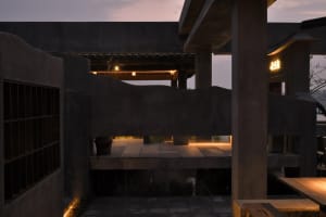 A modern building with a stone and concrete facade, featuring a staircase leading to a patio area with two potted plants, creating a calm and inviting atmosphere