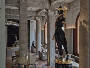 A grand dining room with an ornate statue on a pedestal, surrounded by chairs and a dining table, in a luxurious interior design setting
