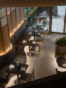 A cozy restaurant interior with multiple dining tables and chairs, wine glasses, and comfortable seating for patrons