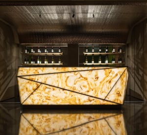 A well-lit bar area with a marble countertop, wine bottles, and a sophisticated atmosphere