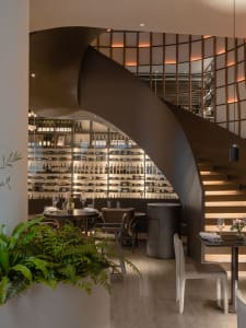 Elegant restaurant interior with a spiral staircase, wooden stairs, metal railing, and wine glasses displayed throughout the space