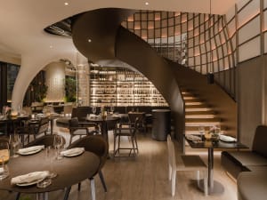 Modern restaurant interior with a spiral staircase, wooden stairs, and comfortable seating areas with tables and chairs, wine glasses, and a focus on functionality and comfort