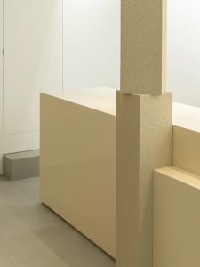 A modern interior space with a white wall, a concrete pillar, and two benches in a symmetrical arrangement, giving a clean and bright appearance