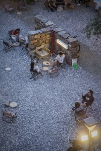A casual outdoor gathering with several people seated around a dining table on a gravel surface