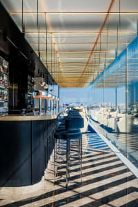 Modern bar area with a wooden counter, stools, and chairs, featuring bottles and a stylish atmosphere