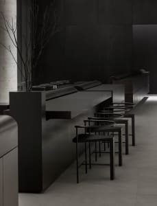 Dark and moody restaurant interior with black walls, a countertop, and chairs placed around the dining area