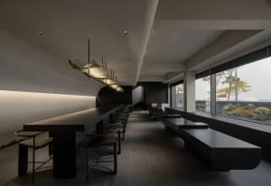 Spacious restaurant dining area with a large table and chairs, concrete walls, and dim lighting