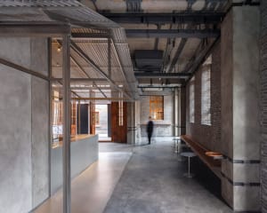 A spacious industrial-style hallway with concrete walls and floors, featuring multiple rooms and benches for seating
