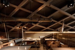 Modern restaurant interior with wooden tables, metal accents, and a warm atmosphere, featuring a dining area with a bar and comfortable seating