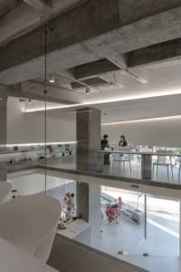 Bright and inviting open concept space with glass walls, concrete surfaces, and white accents, featuring people and furniture