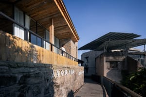 Asian-style building with a stone wall, wooden deck, and balcony, set in a peaceful rural environment