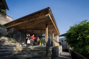 A group of people stand outside an old wooden building with a rustic charm, surrounded by natural surroundings