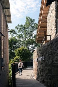 An Asian woman walks down a stone pathway in a courtyard with a mix of stone and wood architecture, surrounded by trees and a sense of tranquility