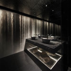 Luxurious bathroom with a large sink featuring two bowl basins, surrounded by black marble countertops and two separate shower areas