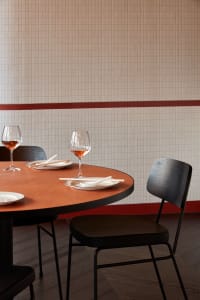 Empty dining area with a round wooden table, tile wall, and three wine glasses with red liquid