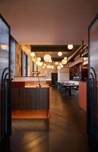 A modern restaurant interior with wooden floors and walls, featuring dining tables and chairs in a warm and inviting atmosphere