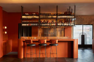 A warm and inviting bar area with a wooden counter, stools, and wine glasses, surrounded by bottles of various beverages