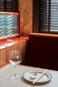 Cozy restaurant dining area with a wooden table, two chairs, a wine glass, and a bowl with a spoon, set for a meal