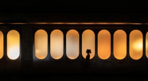 Interior view of a building through a glass door with three arches, a woman standing outside admiring the design