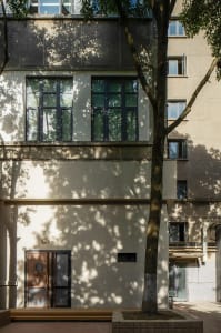 A modern building with a concrete exterior, large windows, and a flat roof, surrounded by trees in a urban environment