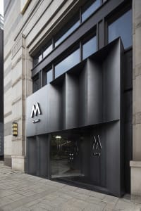 Modern lobby entrance with a glass door, metal frame, and potted plants, featuring clean lines and minimalistic design elements