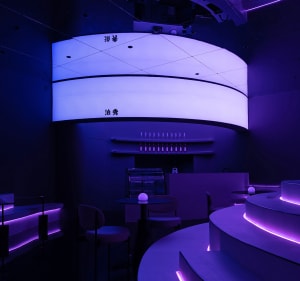 A modern bar area with purple walls, a dining table, chairs, and a refrigerator, creating a comfortable and inviting atmosphere