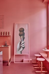 A bright and cheerful room with a large pink wall featuring a fun ice cream poster, two chairs, and a sink, creating a playful atmosphere