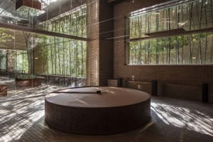 A calm and inviting interior space with a large wooden circular structure, surrounded by windows, and two benches, one on each side