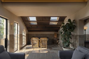 A warm and inviting living area with a dining table under a skylight, surrounded by chairs and a potted plant, with natural light filling the space
