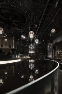A modern bar with a long counter, mirror, and seating areas, featuring scattered bottles and a stylish atmosphere