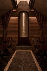Warm and inviting restaurant interior with wooden floors and walls, featuring two dining tables with chairs and a cozy atmosphere