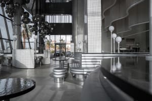 Modern restaurant interior with multiple dining tables and chairs, white and grey tones, and clean lines