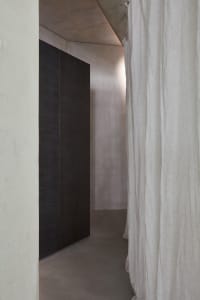 A dimly lit hallway with two black doors, one open, and elegant curtains in the background