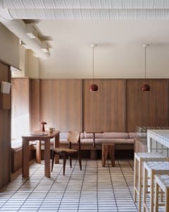 Well-lit living area with a dining table, chairs, couches, and a kitchen counter, featuring wooden floors and walls, and two chandeliers