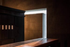Dimly lit room with a wooden cabinet, concrete walls, and natural light from two windows