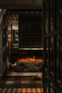 Warm and inviting living space with a stone and glass fireplace, surrounded by a black frame, and a rock wall, featuring two chairs and a dining table