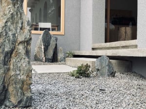 A serene outdoor space in front of a building features a rock garden with large rocks and a set of steps leading to the entrance