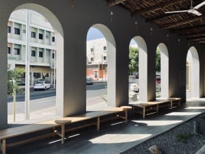 A well-lit outdoor seating area with wooden benches under arches, surrounded by parked cars, creating a welcoming atmosphere