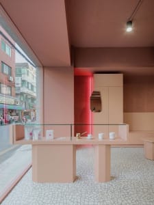 A pink room with a glass display case on a countertop, featuring two cups and a bottle, in a well-lit space